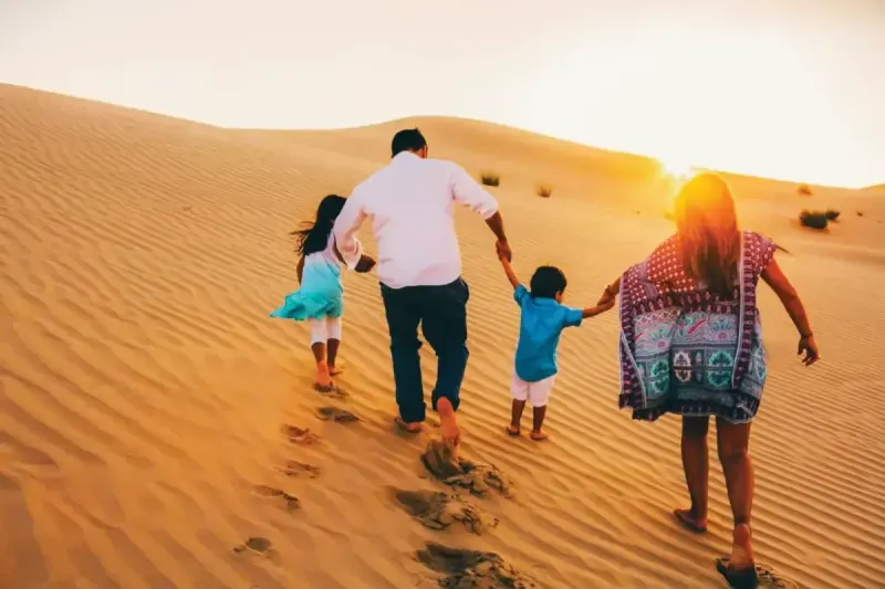 Family walking up a red dune together at sunset on a Dubai desert safari