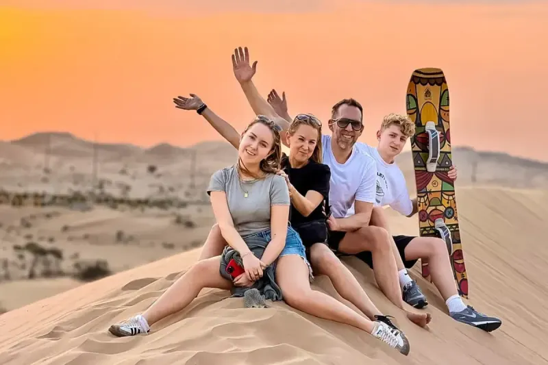 Family with a sandboard on top of a dune during a half day private desert safari in Dubai