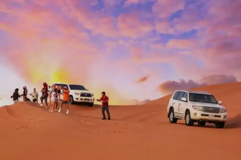 Group of guests watching the sunset beside Land Cruisers on a Dubai desert safari