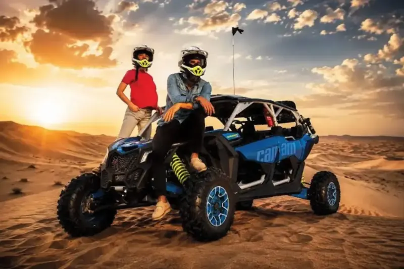 Riders in helmets with a Can-Am Maverick X3 dune buggy at sunset in Dubai