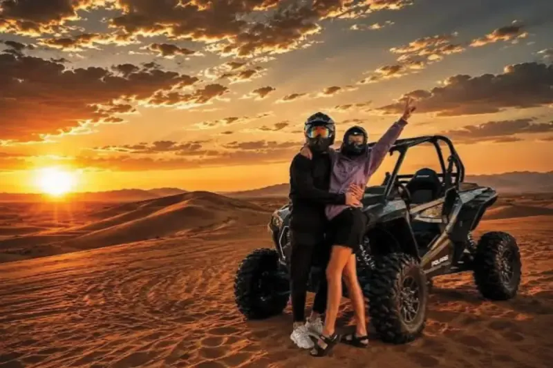 Couple in helmets beside a Polaris RZR dune buggy at sunset in Dubai