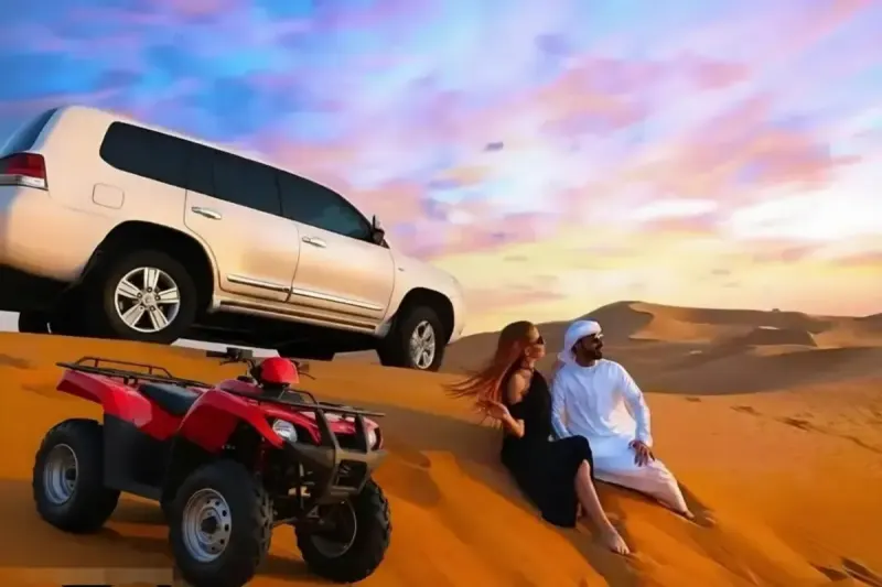 Couple on the dunes next to a red quad bike and Land Cruiser at sunset in Dubai