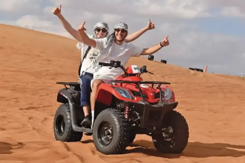 Two riders sharing a red 2 person quad bike in the Dubai desert